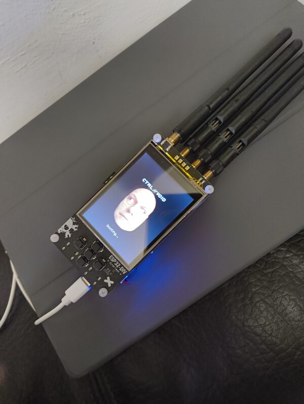 The ESP32-DIV board on a desk, four antennas fanned out to one side and a USB-C cable plugged in, showing the CTRL//VOID boot splash on its screen